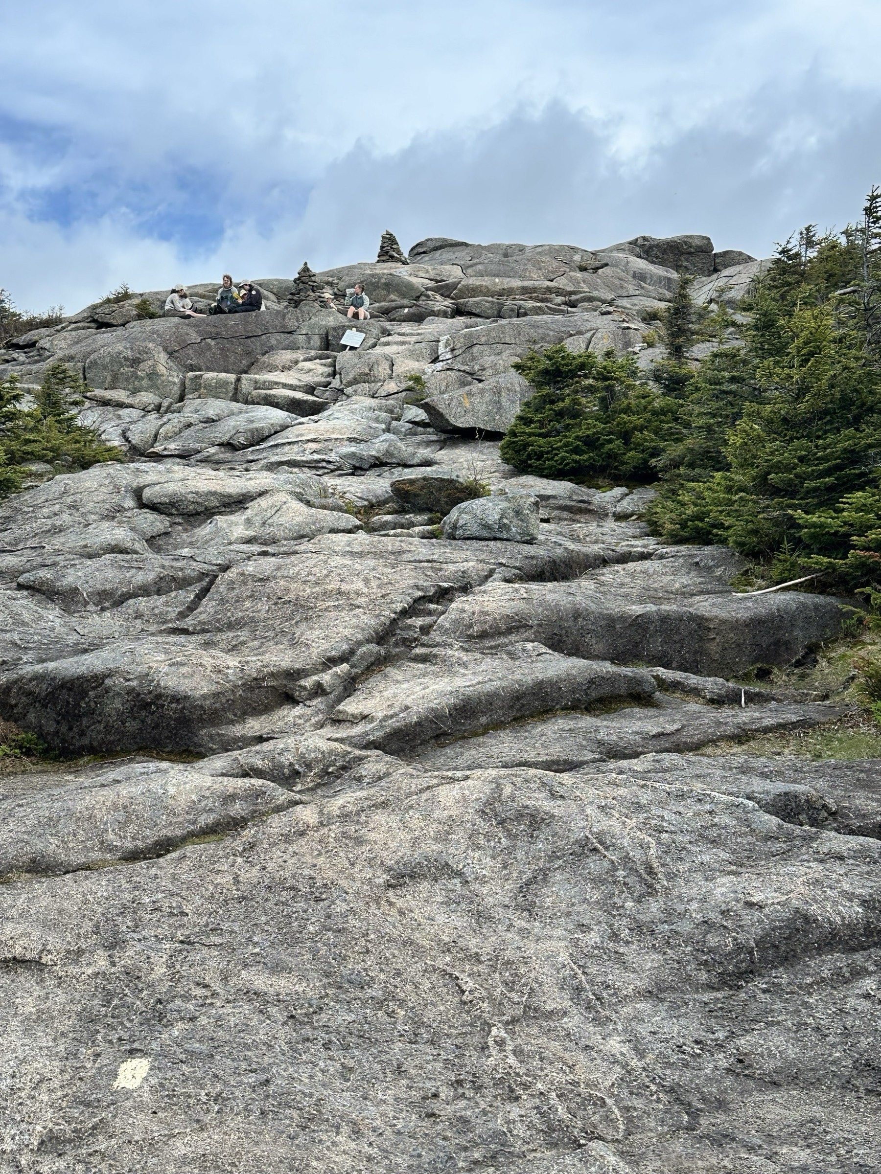 Hikers resting beside the cairn on Cascade's bare-rock summit ridge.